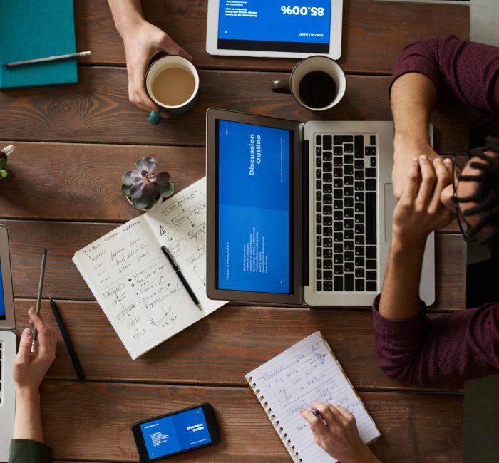 Group of coworkers discussing business strategies with laptops and tablets in a modern office setting.